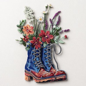 Puede incluir: Una obra de arte bordada que presenta una bota azul y roja llena de flores coloridas. La bota tiene costuras y cordones intrincados, con flores rojas, naranjas y blancas, y follaje verde. La obra está sobre un fondo blanco.