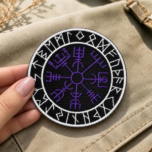 May include: A circular embroidered patch featuring a black background with a purple Vegvisir symbol in the center. The outer border is black with white embroidered runic characters. The patch has a white stitched edge and a textured fabric finish.