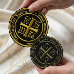 May include: Two round embroidered patches. The patches are black with gold lettering and a gold cross design in the center. The text around the edge of the patches is in a foreign language.