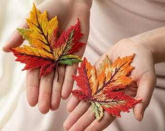 Può includere: Due toppe ricamate a forma di foglia d'acero nei colori autunnali rosso, arancione, giallo e verde. Le foglie sono tenute in mani aperte, mostrando le cuciture dettagliate e le tonalità vivaci. Le toppe sono probabilmente per cucire o creare.