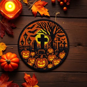 Può includere: Una toppa rotonda a tema Halloween con una scena di cimitero, con lanterne a forma di zucca, una croce e pipistrelli contro una luna gialla. La toppa è nei colori arancione e nero, con una silhouette di albero. La toppa è su una superficie di legno.