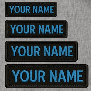 May include: Four black embroidered patches with the text "YOUR NAME" in bright blue. The patches are rectangular with rounded corners and a stitched border. The patches are displayed on a grey textured background.