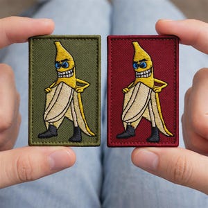May include: Two embroidered patches featuring a yellow banana character with sunglasses and a large grin. The banana is wearing black boots and standing with its peel open. One patch has a green background, the other is red.