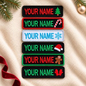 Può includere: Sei toppe rettangolari ricamate con il testo YOUR NAME in vari colori. Le toppe includono icone natalizie: un albero verde, un bastoncino di zucchero rosso e bianco, un fiocco di neve blu, un cappello da Babbo Natale, un omino di pan di zenzero e muffole rosse.