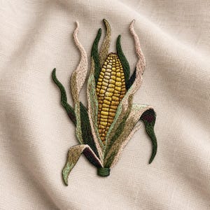 Puede incluir: Un parche bordado que presenta una mazorca de maíz amarilla rodeada de hojas superpuestas en tonos verde oscuro, oliva y rosa pálido. El bordado crea una representación texturizada y detallada del vegetal con bordes de hojas largos.