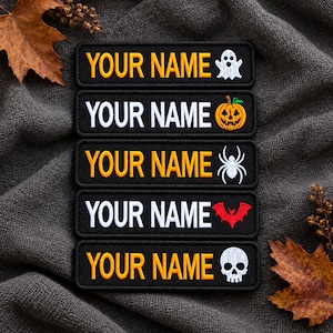 Könnte beinhalten: Fünf rechteckige, schwarze Stickaufnäher mit dem Text YOUR NAME in gelbem oder weißem Garn. Jeder Aufnäher zeigt ein anderes Halloween-Motiv: ein weißes Gespenst, einen orangefarbenen Kürbis, eine weiße Spinne, eine rote Fledermaus und einen weißen Totenkopf.