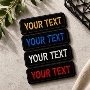 Pode incluir: Quatro emblemas retangulares pretos bordados dispostos verticalmente. Cada emblema apresenta o texto "YOUR TEXT" costurado com uma cor de linha diferente: amarelo, azul, branco e vermelho. Os emblemas têm cantos arredondados e borda preta.