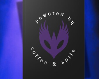 May include: Black notebook with the text "powered by coffee & spite" in white, arched around a purple emblem. The emblem is a stylized design with wing-like shapes. The notebook has a matte finish.
