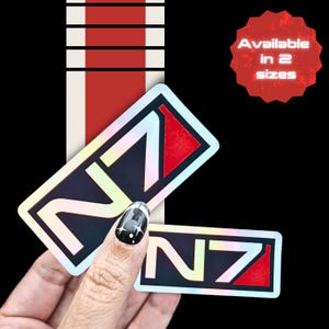 Puede incluir: Dos pegatinas rectangulares con el logotipo N7 y un acabado holográfico. El diseño incluye la letra N y el número 7 en una fuente negrita, con un bloque rojo en el lado derecho. Un gráfico de estrella roja indica Available in 2 sizes.