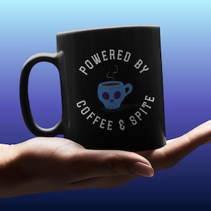 以下が含まれることがあります： 「POWERED BY COFFEE & SPITE」の白文字が入った黒いコーヒーマグ。青いスカル型のコーヒーカップのグラフィックが特徴です。マグカップにはカーブしたハンドルがあり、グラデーションの青い背景に配置されています。