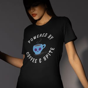 以下が含まれることがあります： 「POWERED BY COFFEE & SPITE」の白文字がプリントされた黒いTシャツ。デザインには、頭蓋骨の顔が付いた青いコーヒーカップが含まれています。このシャツは、クルーネックの半袖です。
