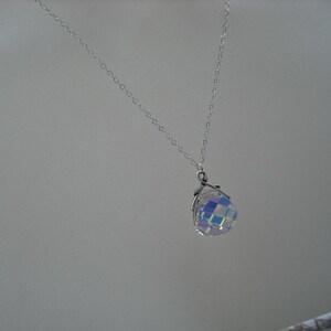 Puede incluir: Un collar de cadena de plata con un colgante de cristal iridiscente. El colgante tiene forma de esfera y un dise&ntilde;o facetado.