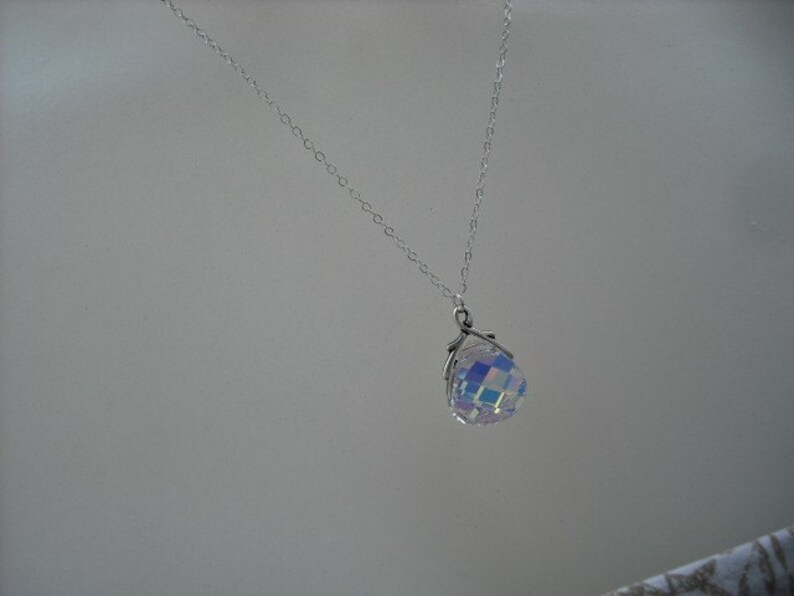 Puede incluir: Un collar de cadena de plata con un colgante de cristal iridiscente. El colgante tiene forma de esfera y un dise&ntilde;o facetado.