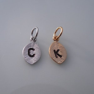 May include: Two silver and gold leaf charms with the letters C and K engraved on them.