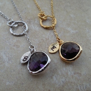 May include: Two delicate necklaces with a single, dark purple gemstone pendant. Each necklace features a small, engraved leaf charm and a double circle design at the top.