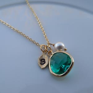 May include: A gold chain necklace with a green gemstone pendant, a small pearl charm, and a gold leaf charm with the letter "B" engraved on it.