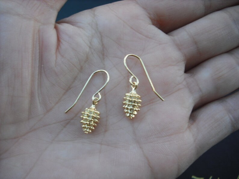 May include: A pair of gold-toned earrings with a small, textured, pine cone-shaped design.