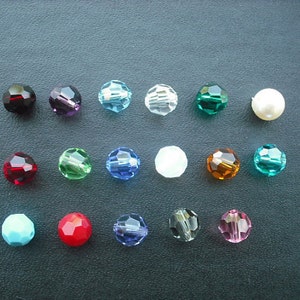 May include: Assortment of 15 round glass beads in various colors, including red, blue, green, turquoise, and clear. The beads are arranged in rows on a dark surface.