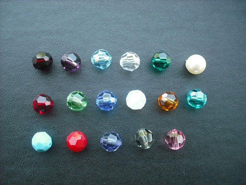 May include: Assortment of 15 round glass beads in various colors, including red, blue, green, turquoise, and clear. The beads are arranged in rows on a dark surface.