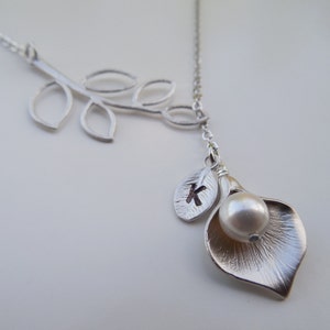 May include: Silver necklace with a delicate branch design and a single calla lily charm with a pearl and a letter K.