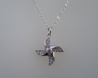 May include: A silver necklace with a small, clear crystal pinwheel pendant.
