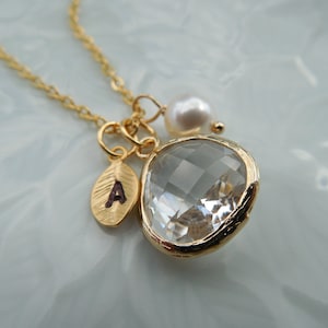 May include: Gold necklace with a clear crystal pendant, a small gold leaf charm with the letter A, and a white pearl charm.