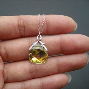 Puede incluir: Un collar de cadena de plata con un colgante de cristal amarillo en forma de l&aacute;grima. El colgante tiene un engaste de plata con un dise&ntilde;o delicado.