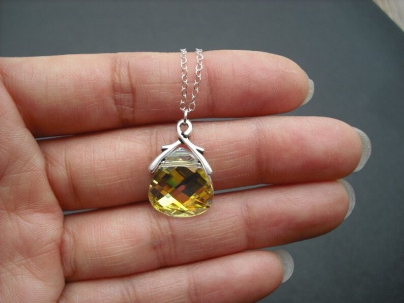 Puede incluir: Un collar de cadena de plata con un colgante de cristal amarillo en forma de l&aacute;grima. El colgante tiene un engaste de plata con un dise&ntilde;o delicado.