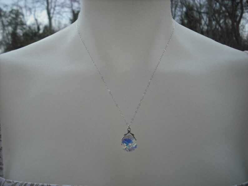Puede incluir: Un collar de cadena de plata con un colgante de cristal iridiscente.