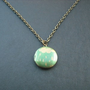 May include: A bronze chain necklace with a round locket featuring a green cloud with gold raindrops.