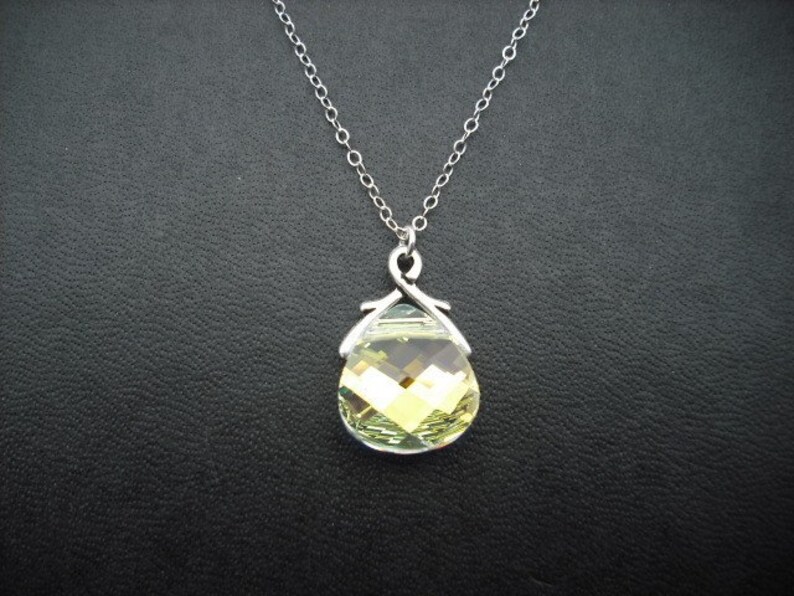 Puede incluir: Un collar de cadena de plata con un colgante en forma de l&aacute;grima con un cristal verde claro facetado.