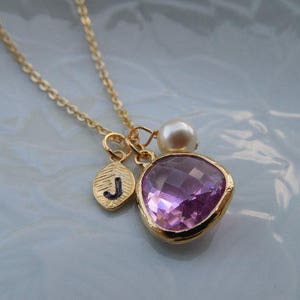 May include: A gold chain necklace with a pink gemstone pendant, a small gold charm with the letter 'J' and a white pearl charm.