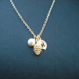 May include: A gold chain necklace with a small pearl, a gold pine cone charm, and a gold leaf charm with the letter "H" engraved on it.