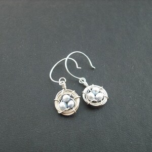 May include: A pair of silver earrings with a wire-wrapped nest design. Each nest contains three small, light gray pearls.