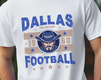 Op de afbeelding: Wit T-shirt met een blauw en bruin grafisch ontwerp met de tekst "Dallas Ride for Glory 19 60 Football" met vijf sterren onder de tekst.