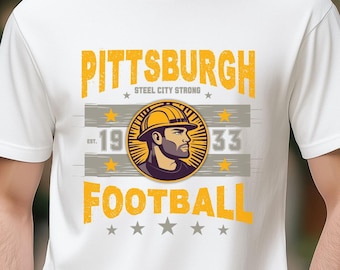 May include: White t-shirt with a yellow and grey graphic design featuring the text "Pittsburgh Steel City Strong" and "Football" with a cartoon image of a man wearing a hard hat.