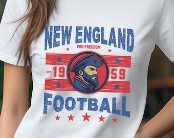 以下が含まれることがあります： 「New England Football」と書いてある赤、白、青のグラフィックデザインが施された白いTシャツ。海賊のイラストと「19」と「59」の年号が描かれている。