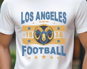 Op de afbeelding: Wit T-shirt met een blauwe en gele grafische print met de tekst "Los Angeles We Got Me -1936 Football" met een rammenkoplogo.