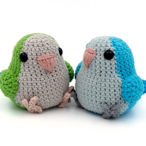 May include: Two crocheted stuffed birds, one green and gray, the other blue and gray, with black eyes and pink beaks.