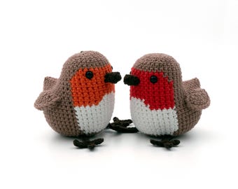 May include: Two handmade crochet birds with brown bodies, orange and red breasts, white bellies, and black beaks and feet. The birds are facing each other, showcasing their detailed craftsmanship. A charming, whimsical decorative item.