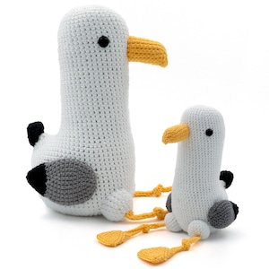 Puede incluir: Dos peluches de gaviota de crochet, uno más grande que el otro. La gaviota más grande es blanca con detalles grises y negros, mientras que la gaviota más pequeña es blanca con detalles grises. Ambas gaviotas tienen picos amarillos y ojos negros.