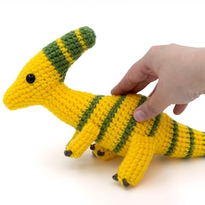 May include: A yellow and green striped crocheted dinosaur toy. The dinosaur has a long neck and a small head with a black eye.