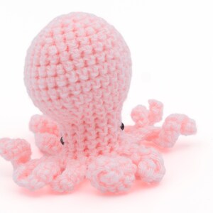Puede incluir: Un pulpo de crochet rosa con ojos negros. El pulpo tiene ocho tentáculos y está hecho de hilo suave.