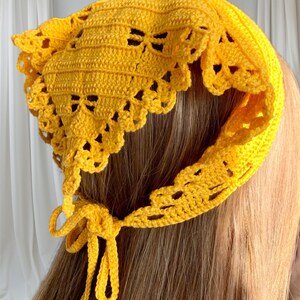 K&ouml;nnte beinhalten: Ein leuchtend gelbes H&auml;kelh&auml;ubchen. Das H&auml;ubchen hat einen gewellten Rand und eine Schleife. Die H&auml;kelarbeit hat ein offenes, zartes Design. Das H&auml;ubchen wird auf einer Person mit langen, hellbraunen Haaren gezeigt.