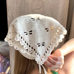 K&ouml;nnte beinhalten: Ein cremefarbenes H&auml;kel-Kopftuch mit Schleifenmuster. Das Kopftuch hat einen dekorativen, gewellten Rand und Bindeb&auml;nder. Es besteht aus weichem, strukturiertem Garn. Ein modisches Accessoire.