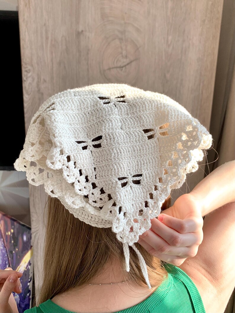 K&ouml;nnte beinhalten: Ein cremefarbenes H&auml;kel-Kopftuch mit Schleifenmuster. Das Kopftuch hat einen dekorativen, gewellten Rand und Bindeb&auml;nder. Es besteht aus weichem, strukturiertem Garn. Ein modisches Accessoire.