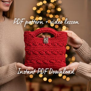 以下が含まれることがあります： 2 人が持っている、ハンドルとシルバーの留め金が付いた赤いかぎ針編みのハンドバッグ。バッグにはテクスチャパターンがあります。画像には「PDF pattern + video lesson」と「Instant PDF Download」というテキストが表示されています。背景はクリスマスの光でぼやけています。