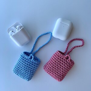 May include: A light blue and a pink crochet case for wireless earbuds, each with a matching strap. Two white earbud cases are also in the image. The cases are handmade and likely designed to protect the earbuds.