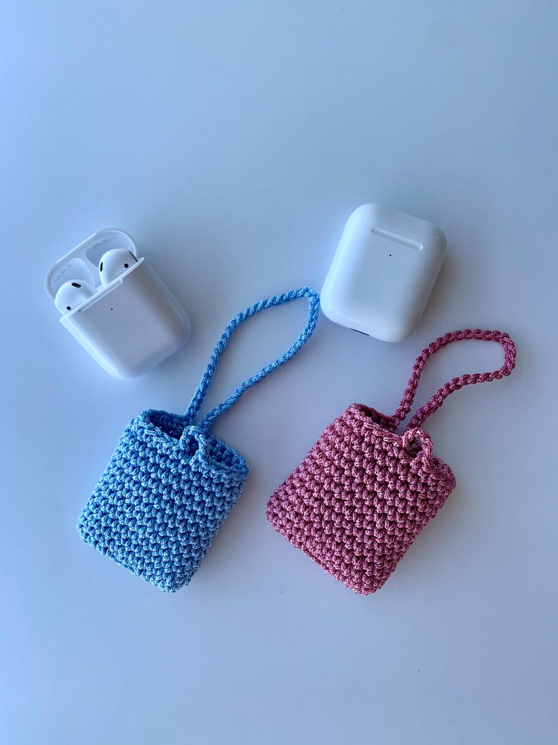 May include: A light blue and a pink crochet case for wireless earbuds, each with a matching strap. Two white earbud cases are also present in the image. The cases are handmade and likely designed to protect the earbuds.