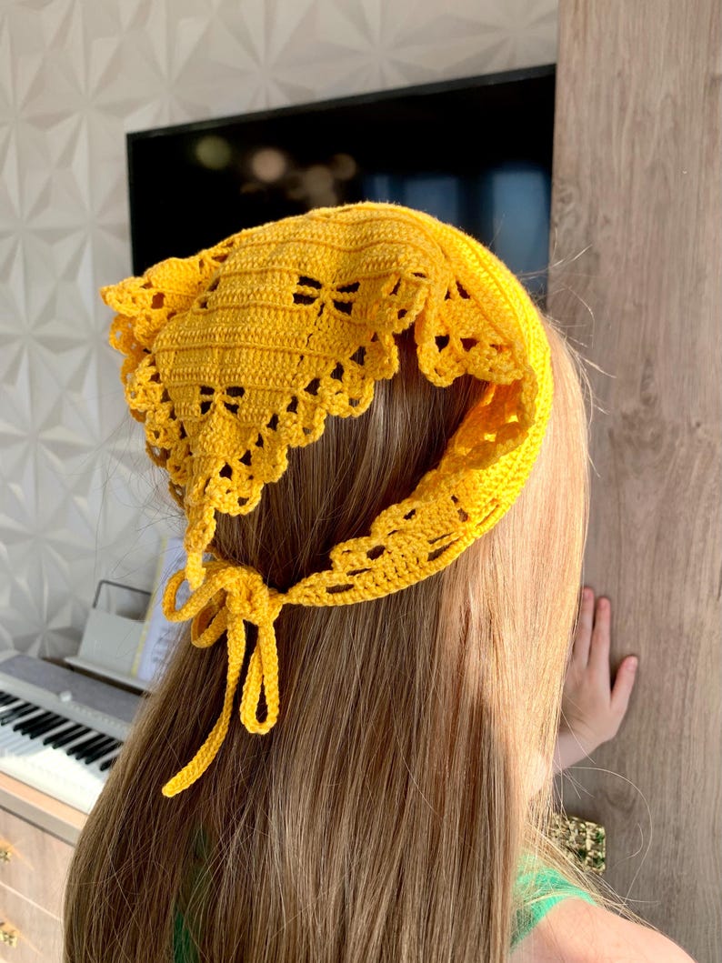 K&ouml;nnte beinhalten: Ein leuchtend gelbes, geh&auml;keltes Kopftuch mit einem gewellten Rand und dekorativen Aussparungen. Die Kopfbedeckung wird am Nacken mit einer passenden gelben Krawatte befestigt. Das Kopftuch ist handgefertigt und scheint aus Baumwollgarn zu bestehen.